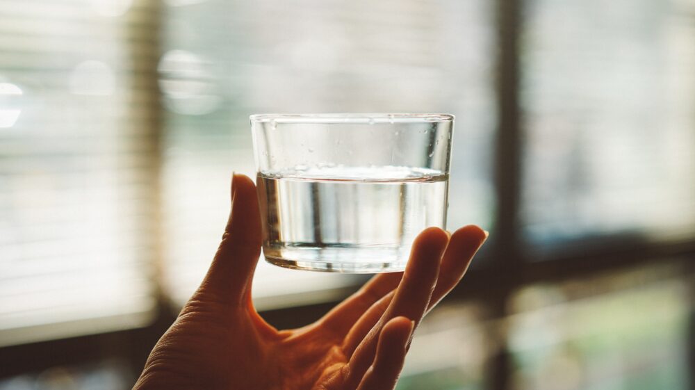 Hand holding clear glass cup with half-filled water, Tokyo, Japan