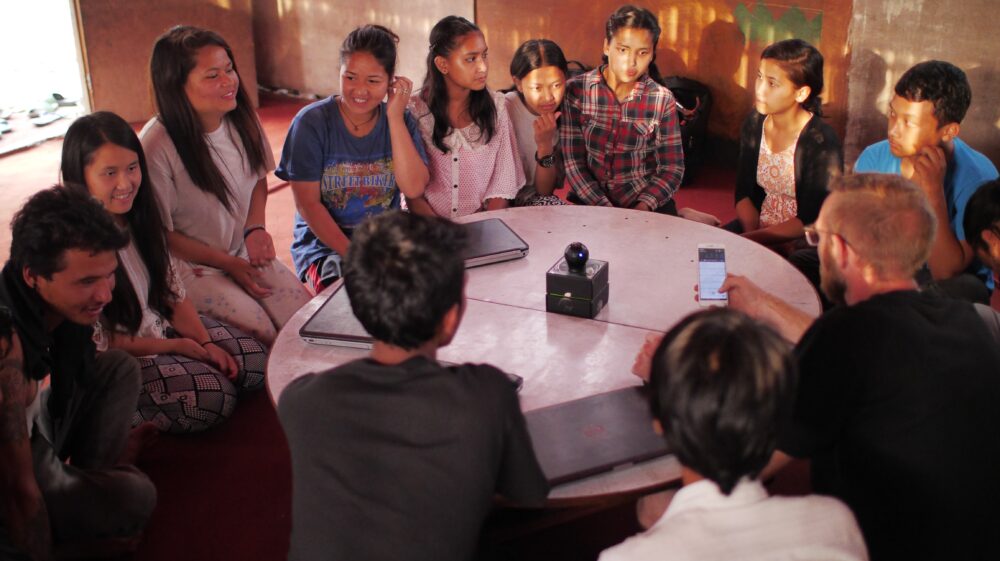 Nepalese youth sit around round table as emergency relief organization Disaster Hack visits Kathmandu slum to demonstrate technological equipment
