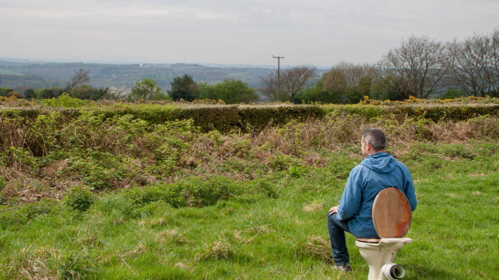 Rear view of man sitting on abandoned toilet in field