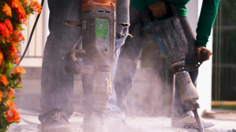 Close-up of construction worker using jackhammer and accompanying dust