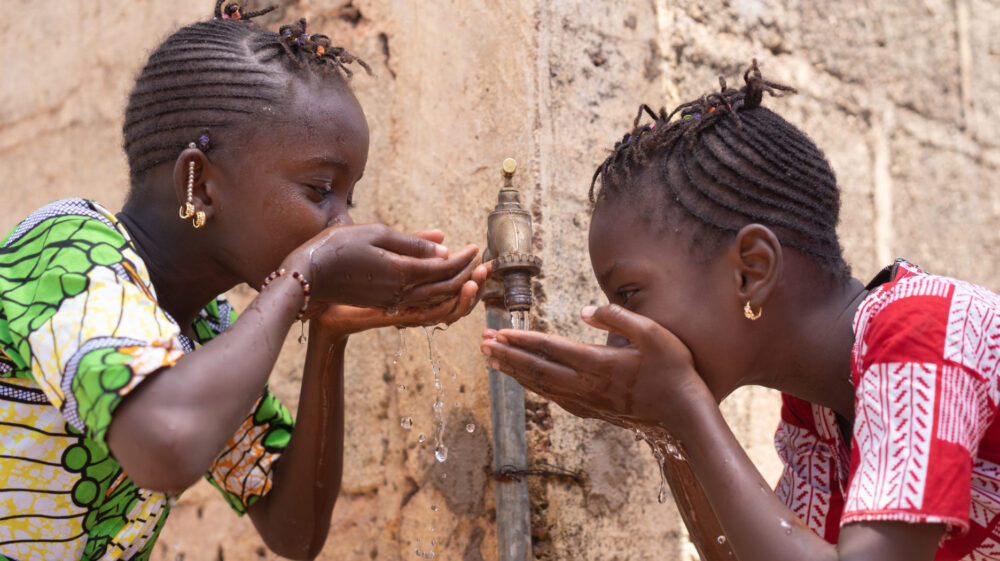Two young Malian girls drinking water straight from a tap, Mali