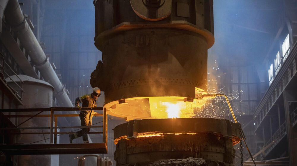 Steelworker inspecting molten steel during steel pour in steelworks, UK