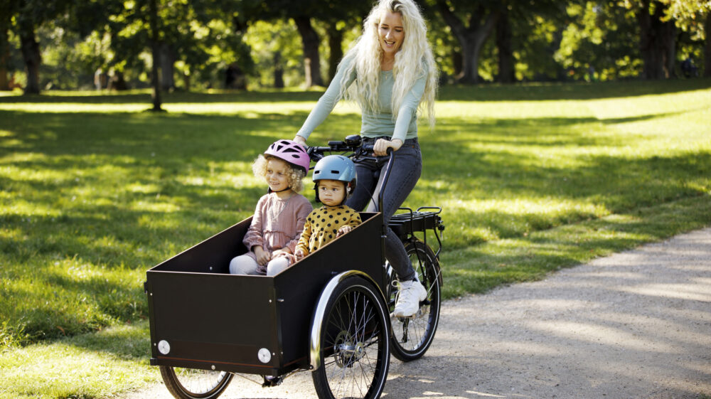 Young mother cycling with two children in electric cargo bicycle
