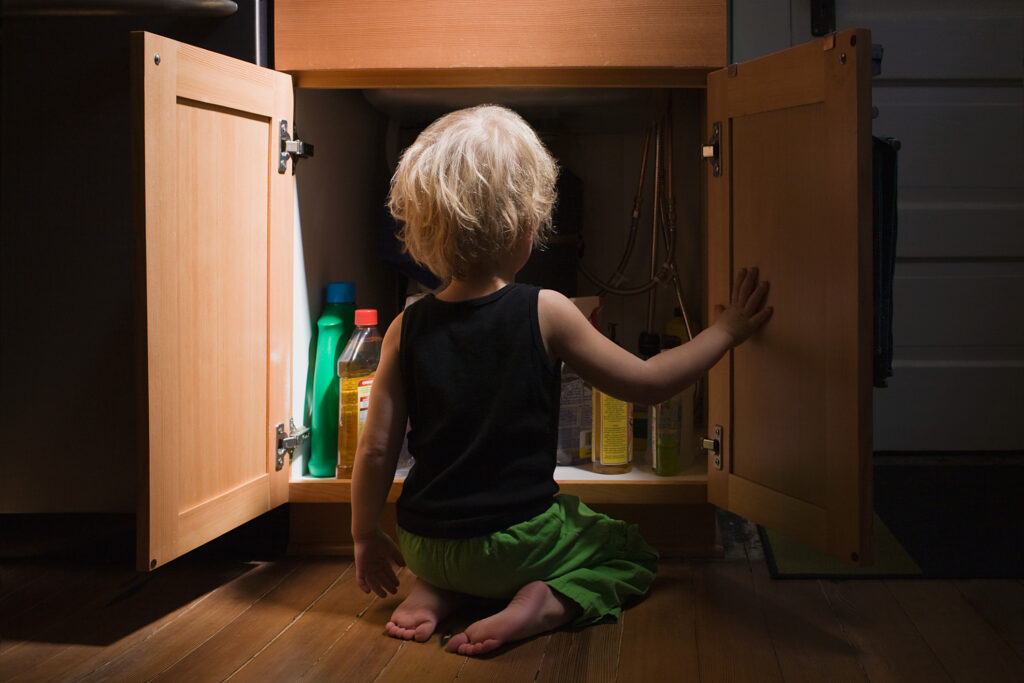 Little boy opening cupboard of cleaning products