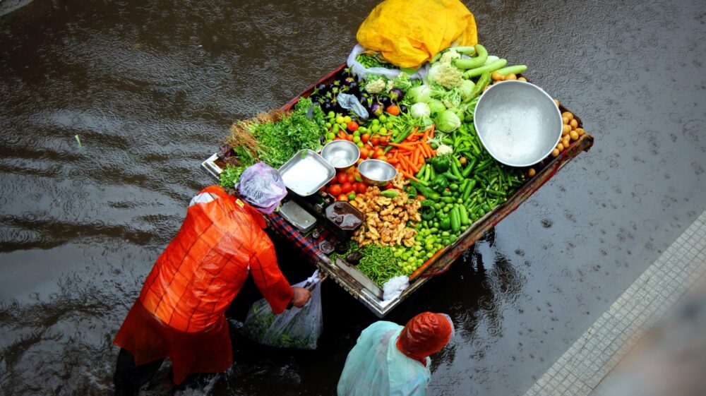 Aerial shot of fruit sellers pushing a cartload of fruit along flooded street during downpour, India