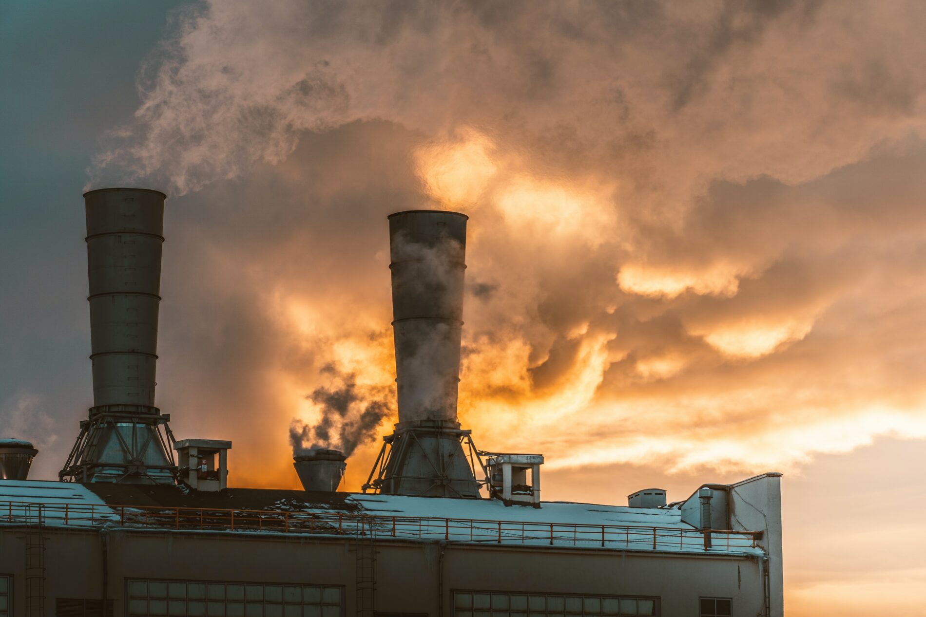Two smokestacks on factory roof with billowing smoke on winter day in overcast sunlight