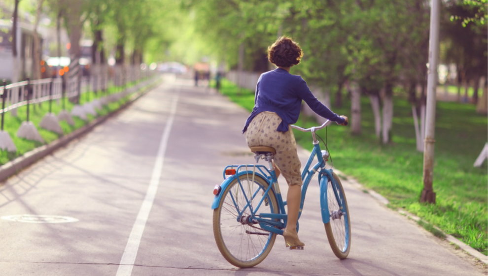 Woman in tan dress and tan heels riding blue bicycle on bike path