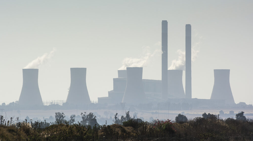 Vapour rises from cooling towers in distance on hazy day with grass in front, Mpumalanga, South Africa