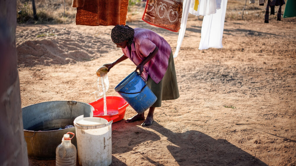 African woman washing clothes in the yard next to the washing line were few blankets are drying