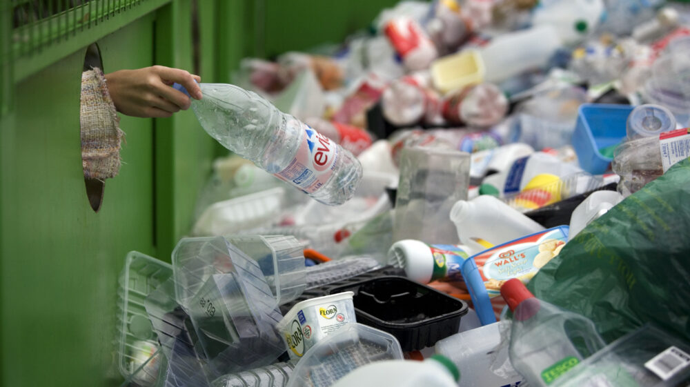 Woman's hand dropping plastic bottle on top of pile of plastic packaging for recycling.