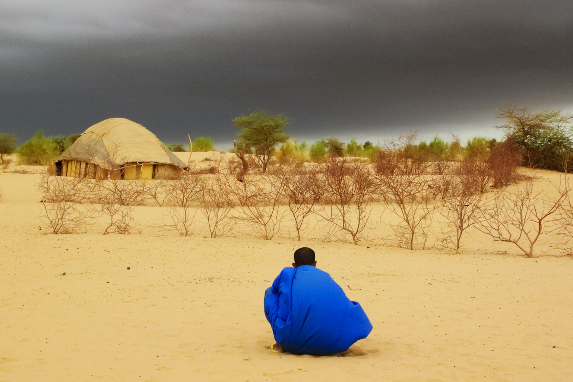 uareg crouching under dark clouds in front of large hut in desert waiting for rain, Timbuktu, Tombouctou, Mali, West Africa