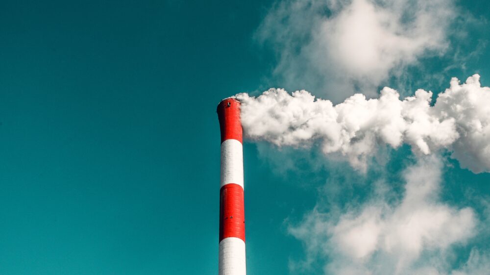 Sky view of factory chimney billowing smoke under blue-green sky