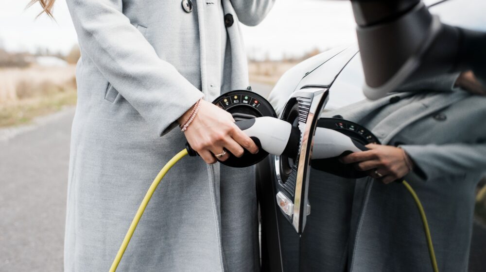 Close-up of woman's hand plugging in charger to electric car, Stockholm, Sweden