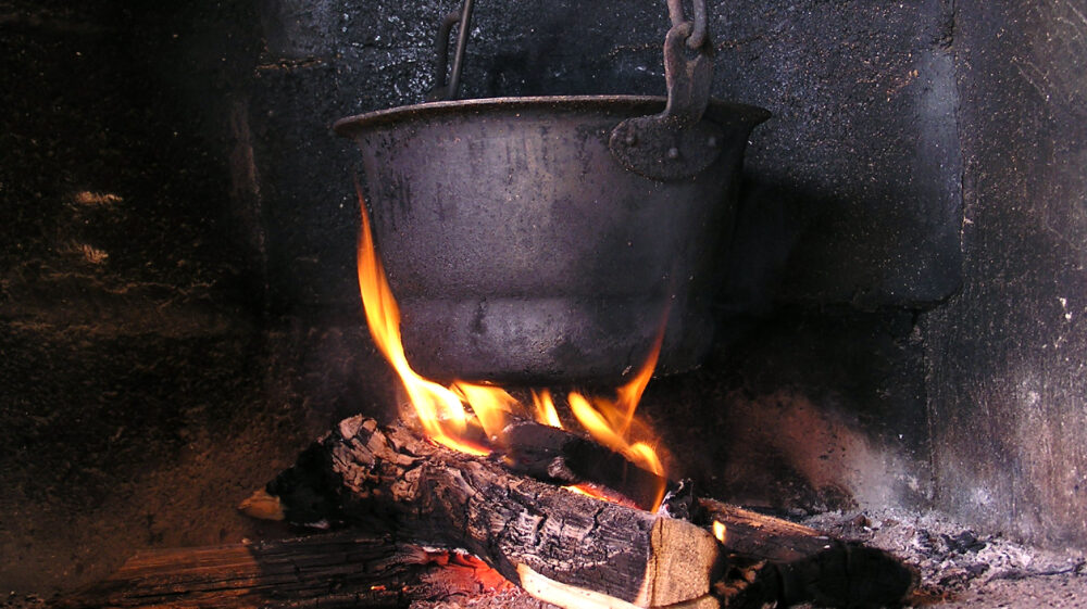 Black pot suspended over wood-burning fire