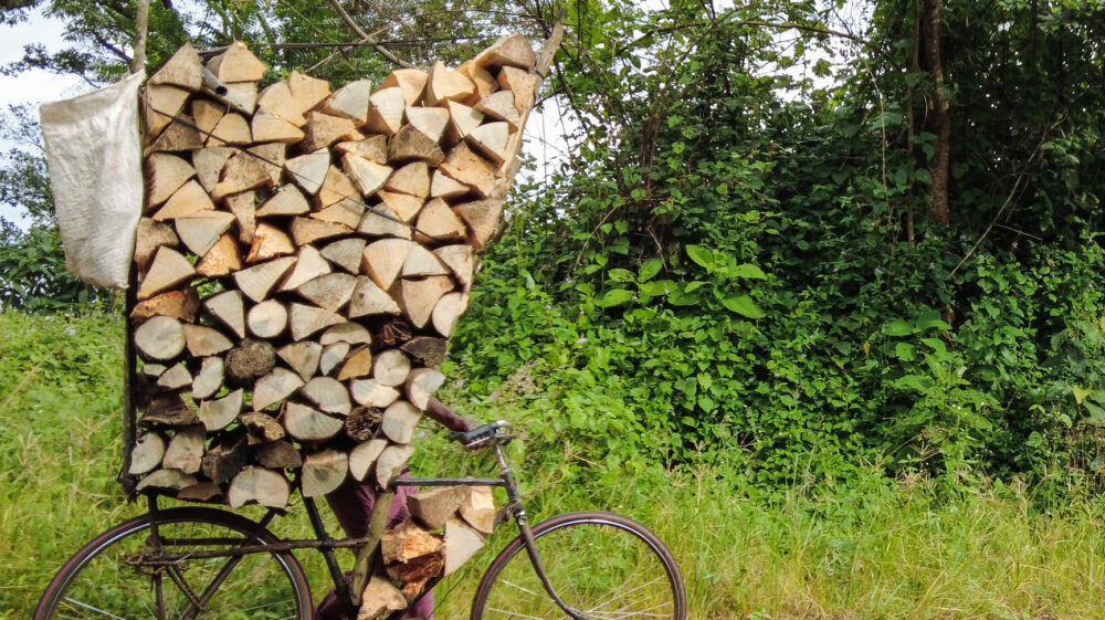 Person transporting tall stack of firewood by bicycle down mountain pass, Zomba, Malawi