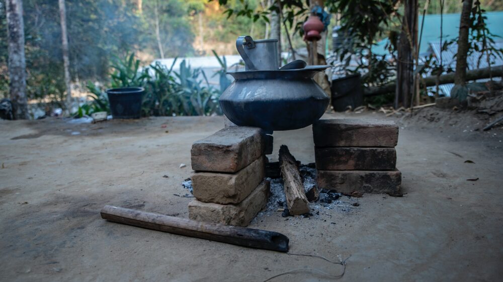 Black clay pot suspended over wood-burning fire, cooking in rural area of Bandarban, Bangladesh
