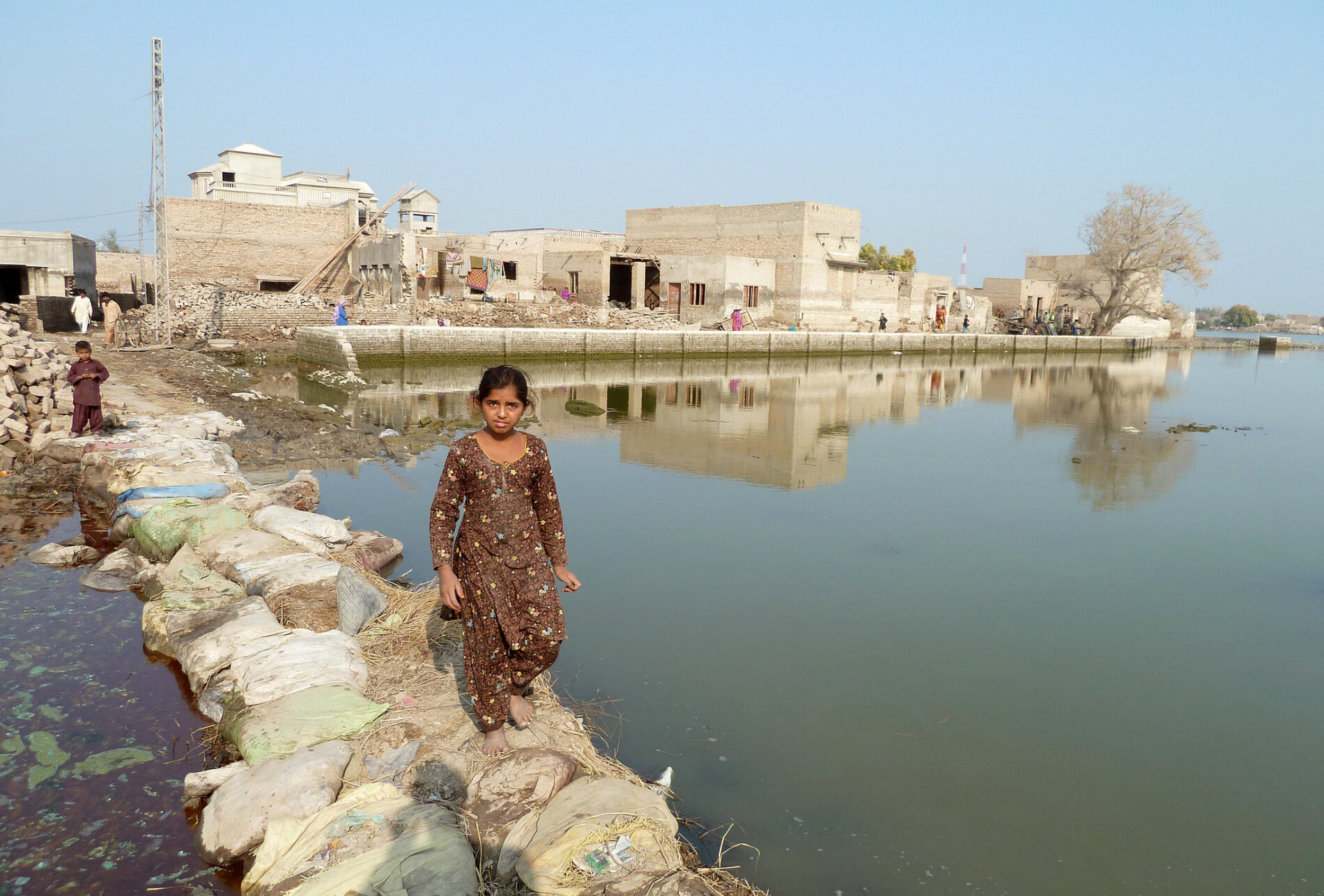 Young girl walks across makeshift bridge over stagnant floodwater in Sindh Province, Pakistan