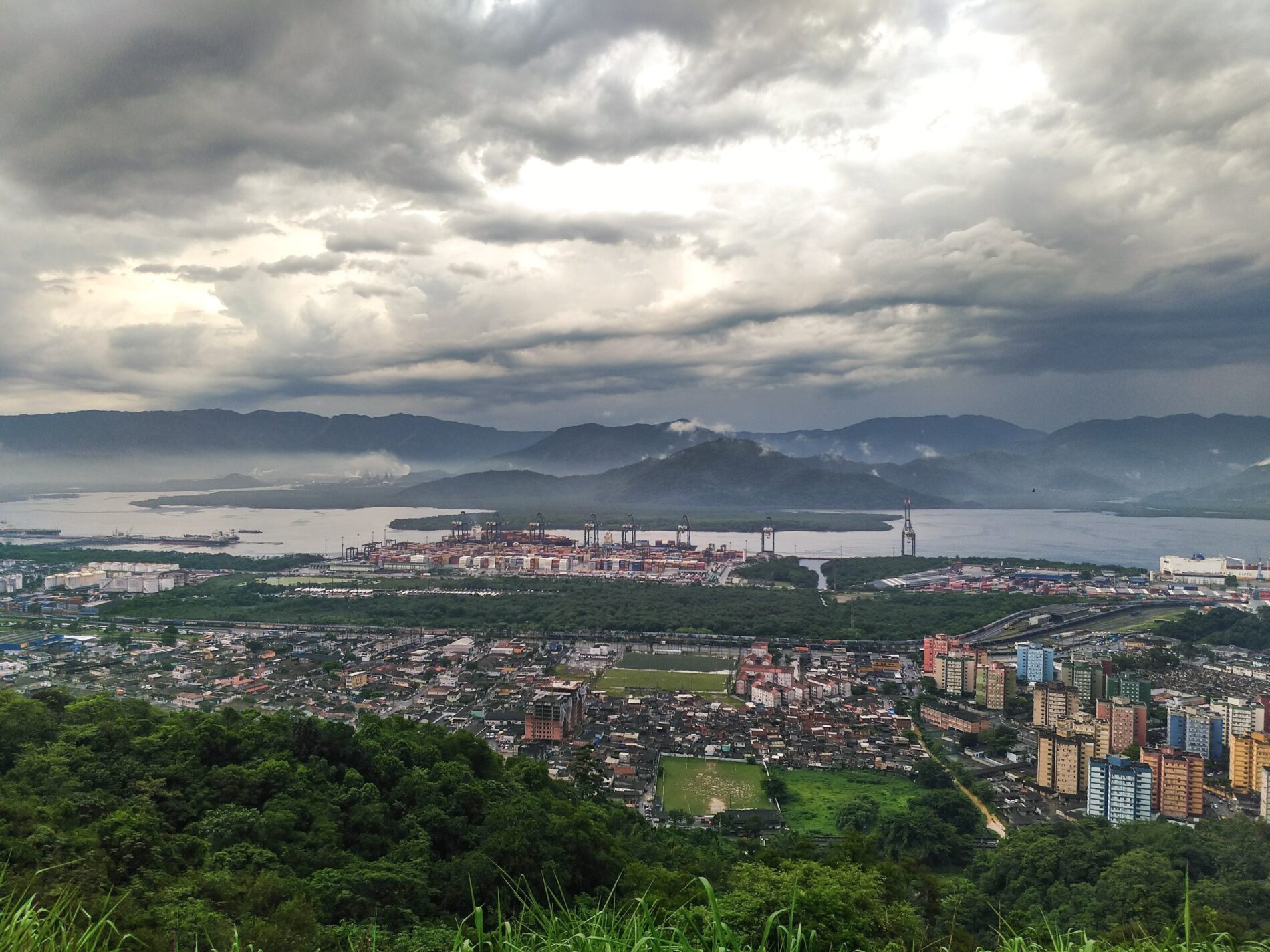 Town with factories and residential buildings with river and mountains in background under overcast sky, Brazil