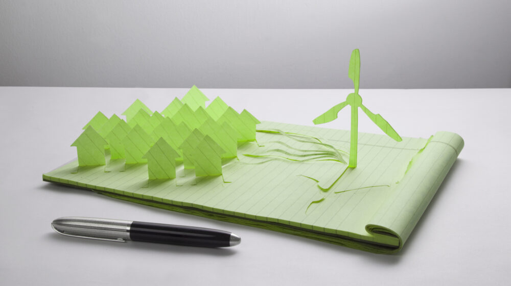 Wind turbine and houses cut from paper on green lined notepad and pen in front