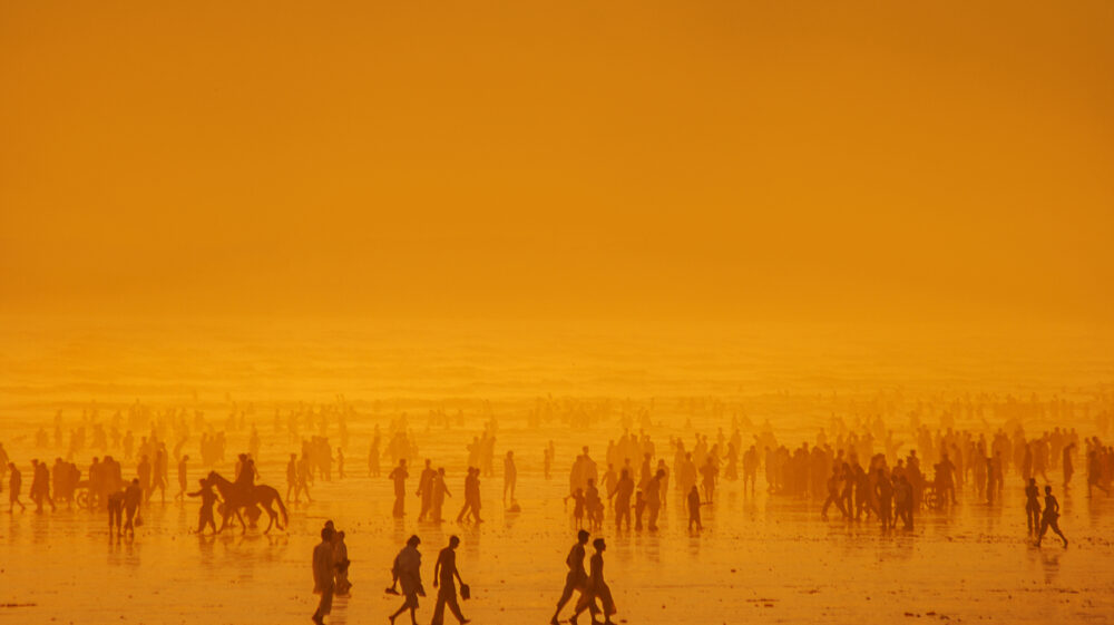Silhouette of crowded beach at sunset with bather riding horse covered in orange fog, Karachi, Sindh, Pakistan