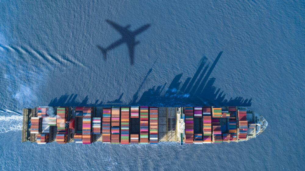 Shadow of aeroplane over water and cargo ship on blue sea