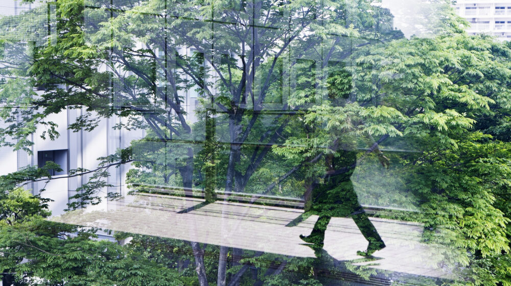 Silhouette of businessman walking along indoor passage reflected through glass with green trees in background, Shinagawa-ku, Tokyo, Japan
