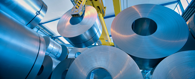 View from ground of coils of freshly rolled steel in plant stacked by yellow crane, Switzerland