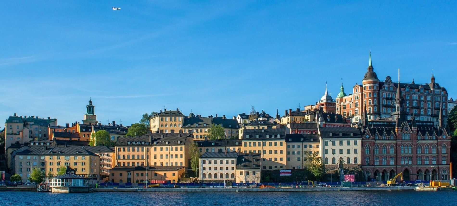 View of Södermalm, Stockholm, Sweden from water and Münchenbryggeriet to the right with plane flying above under blue sky