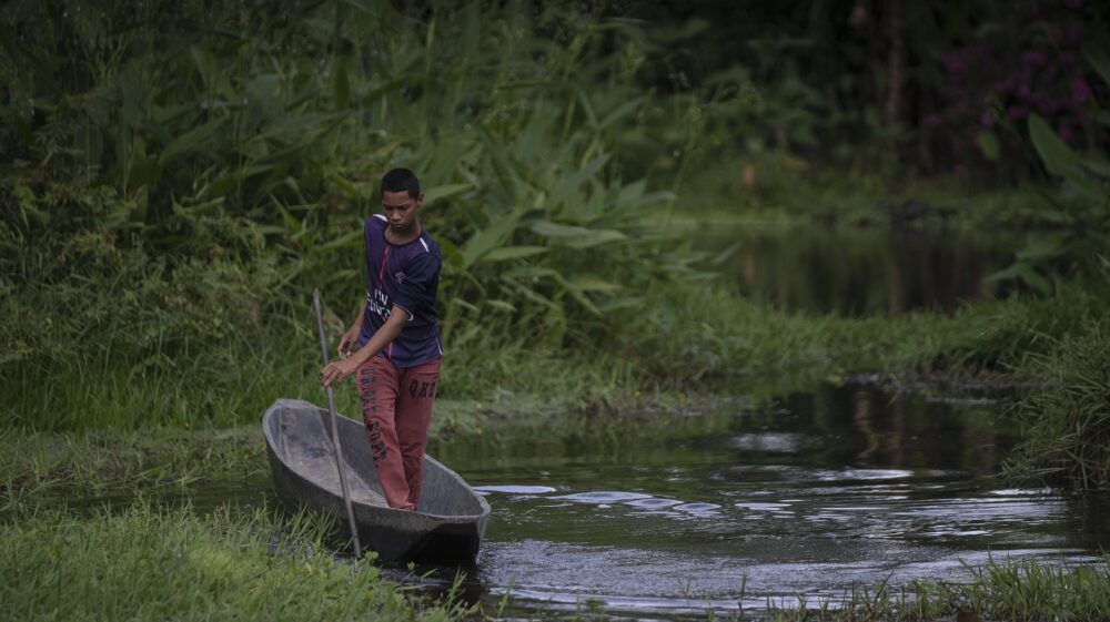 Man paddling rowboat in green swamp