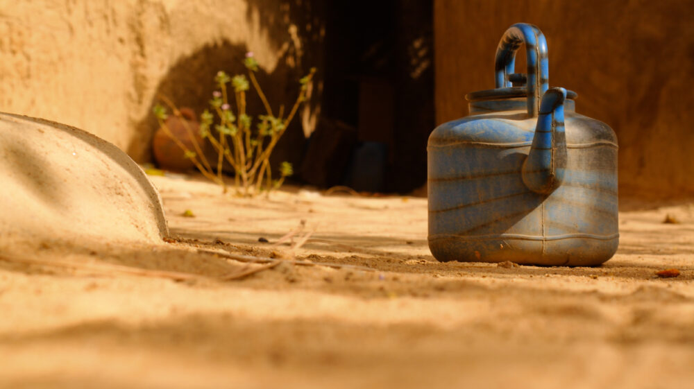 Blue water kettle famous in Mali sits on sandy floor in residential area, Bamako, Mali
