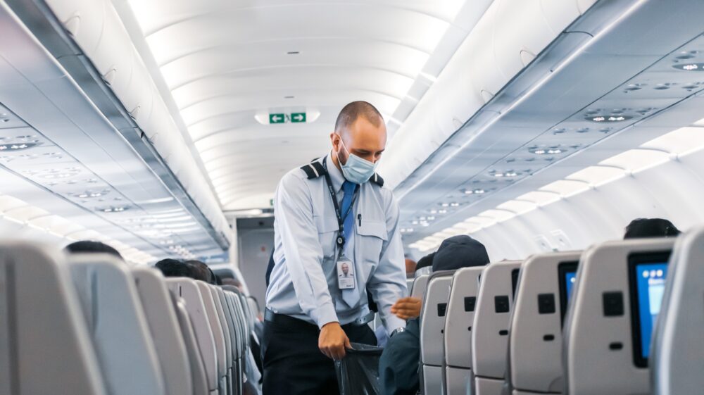 Airport staff wearing face mask collecting garbage on plane, Belo Horizonte International Airport, Confins, Brazil