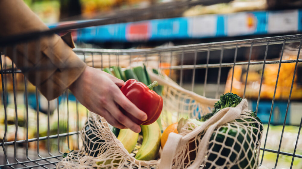 Close-up shot of female hand putting a red bell pepper into mesh reusable grocery bag, UK