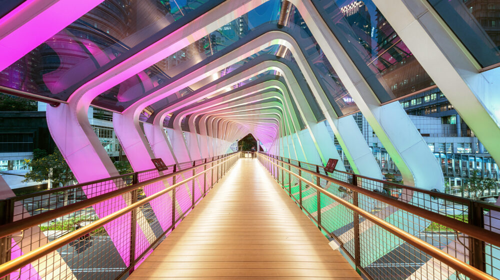 Modern pedestrian bridge crossing Jalan Jenderal Sudirman lit up at dusk in South Jakarta business district, Indonesia