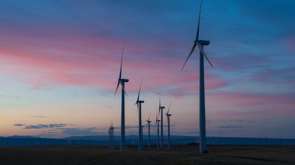 White windmills as tall as 30-story buildings on wind farm at dusk under purple sunset, Columbia Gorge, Wasco, Oregon, USA