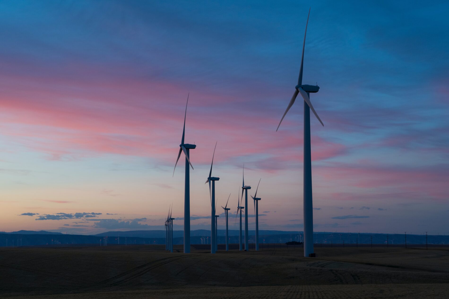 White windmills as tall as 30-story buildings on wind farm at dusk under purple sunset, Columbia Gorge, Wasco, Oregon, USA