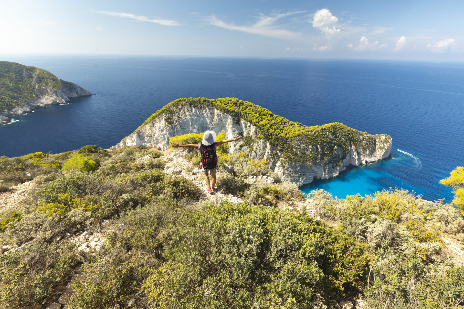 Woman standing arms outstretched and watching at view, rear view of woman standing on top of cliff looking out to sea, Greece