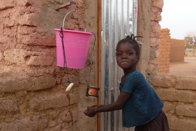 Girl washes hands with water in pink bucket above her