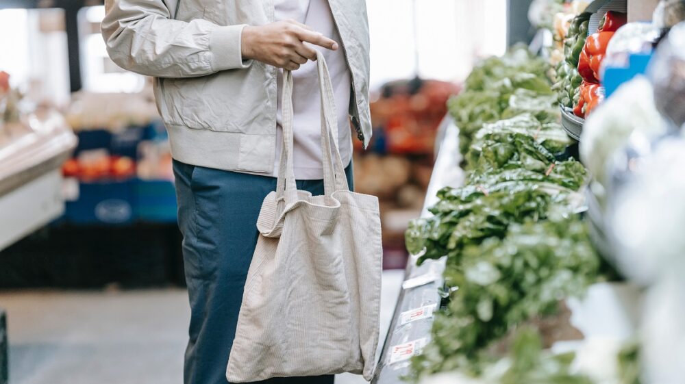 Person shopping with reusable cloth bag in front of green produce