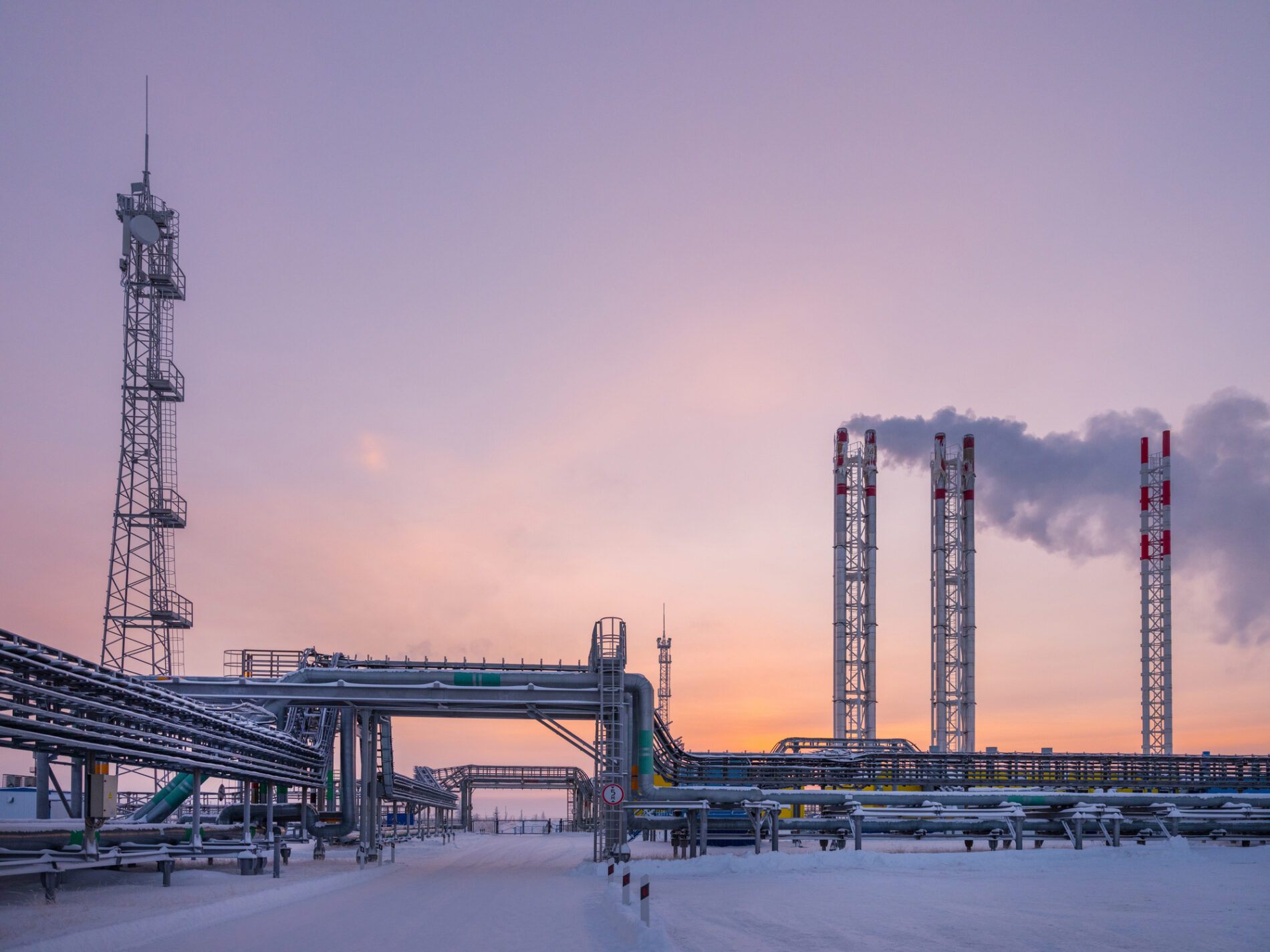Russian gas production and processing facility works under blanket of snow at dawn and cloudy purple and pink sky, Novy Urengoi, Russia