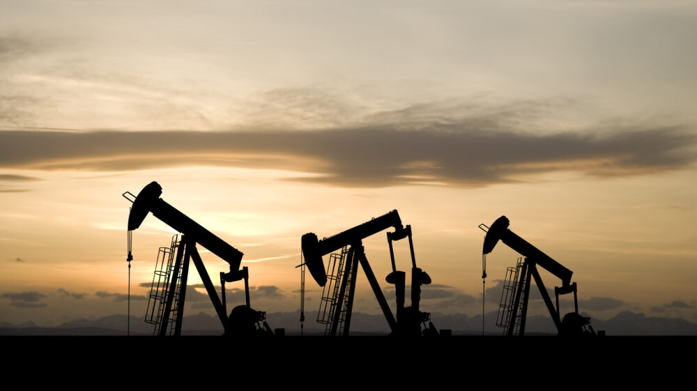 Three oil and gas industry derricks work as sun sets behind them