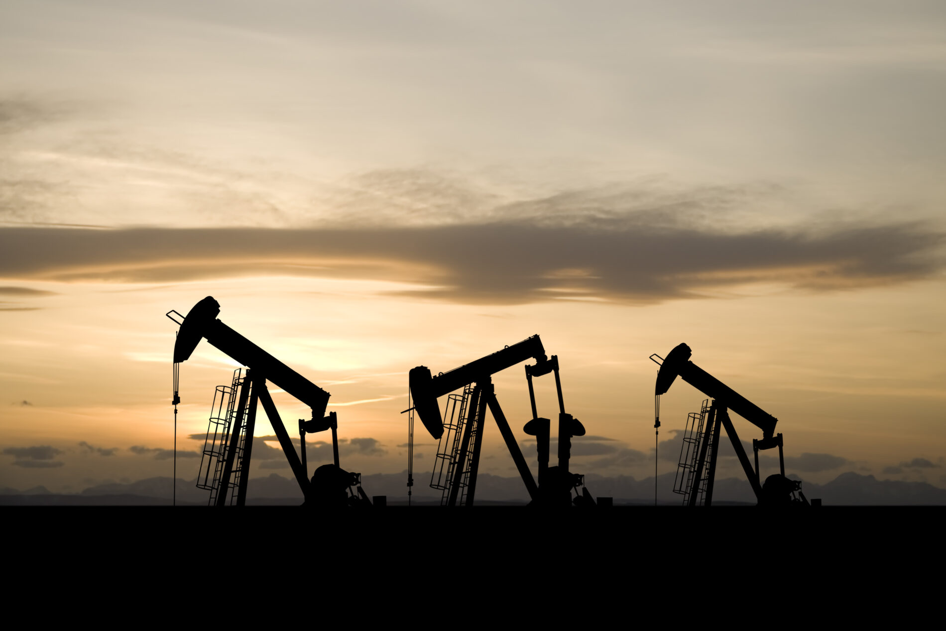 Three oil and gas industry derricks work as sun sets behind them