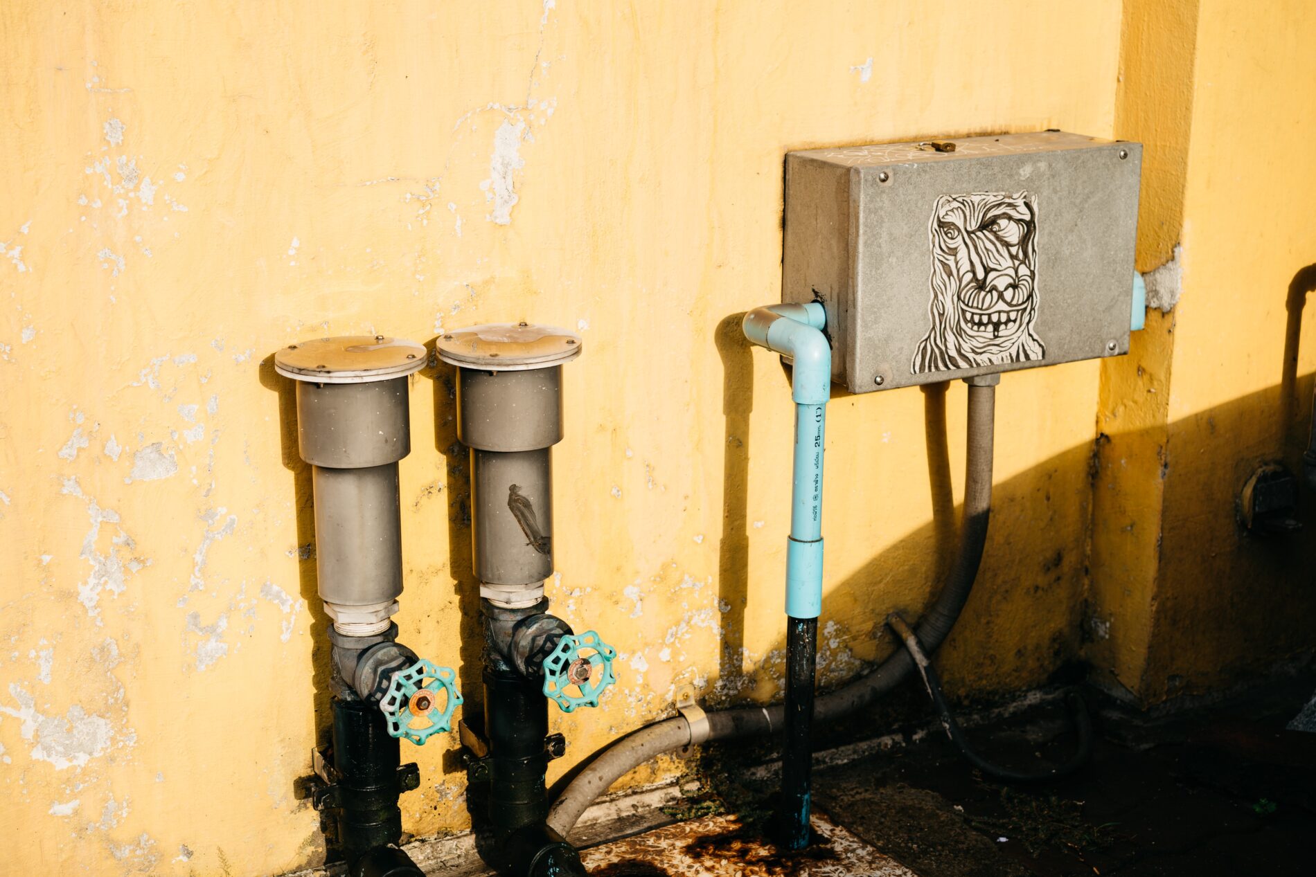 Water meter in building against painted yellow wall and two water pipes with cyan rotary handles, Bangkok, Thailand