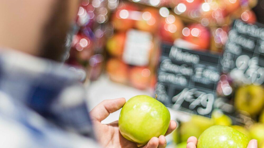 Man holding two green apples in grocery store