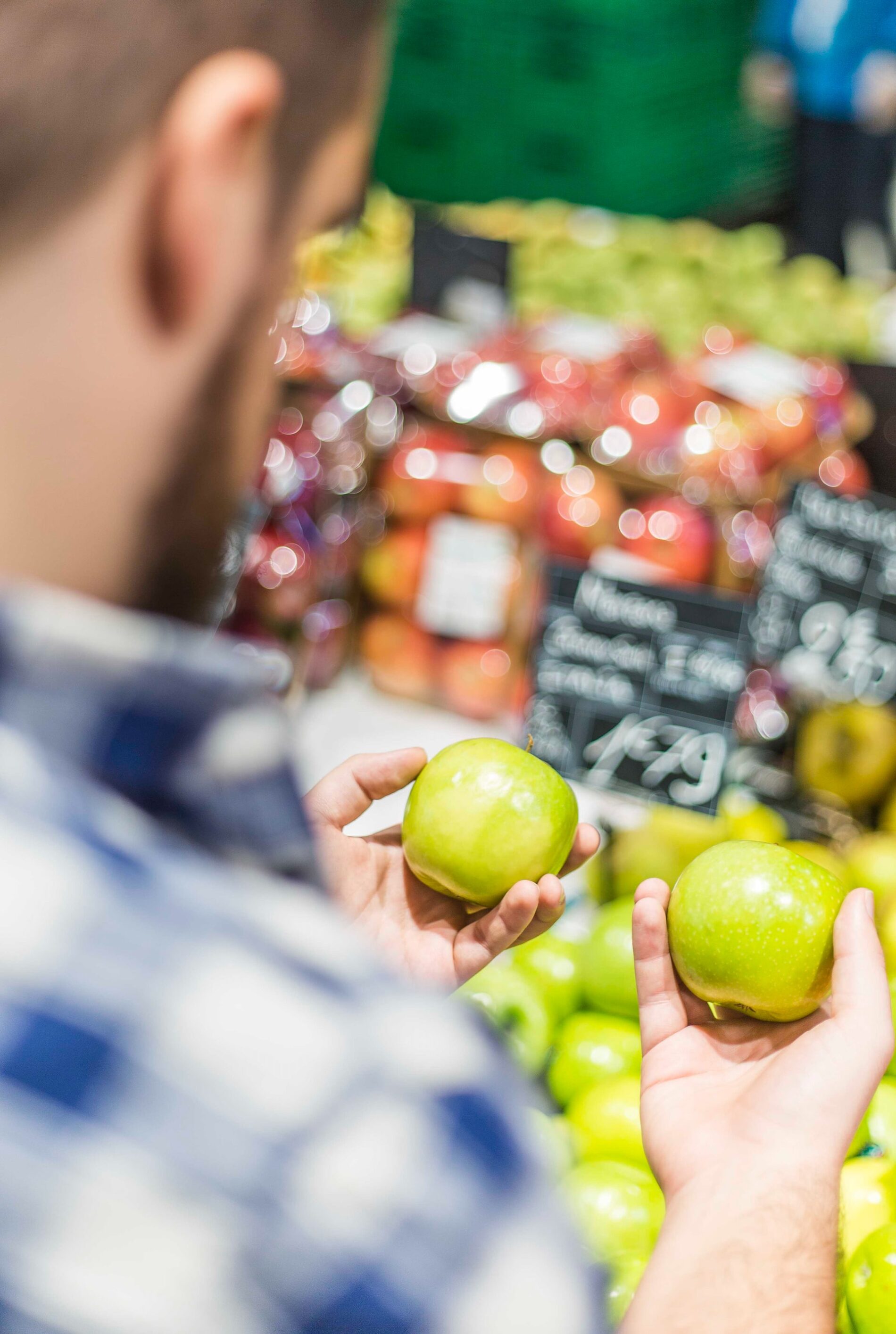 Man holding two green apples in grocery store
