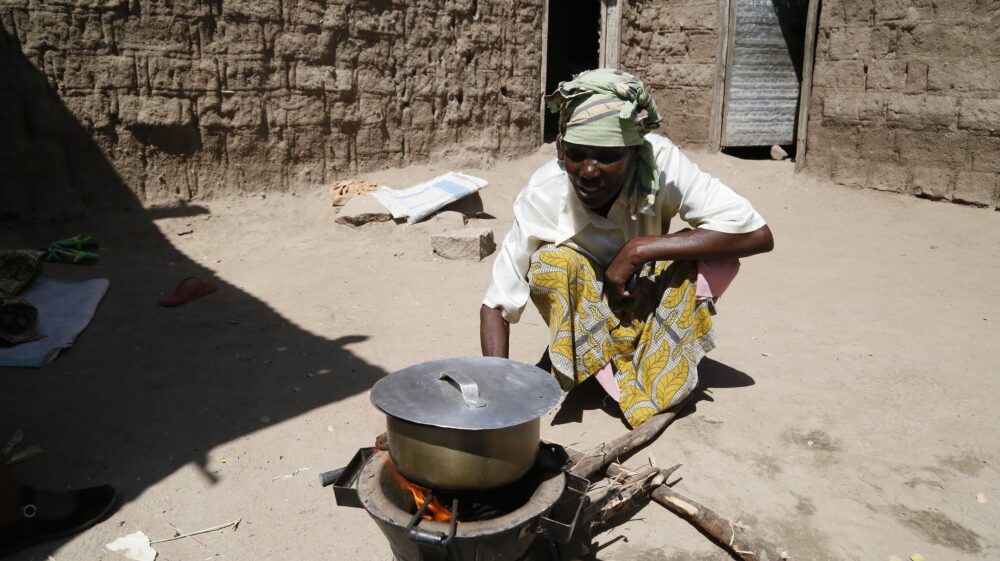Woman sitting next to her cookstove outside her home, cooking food.