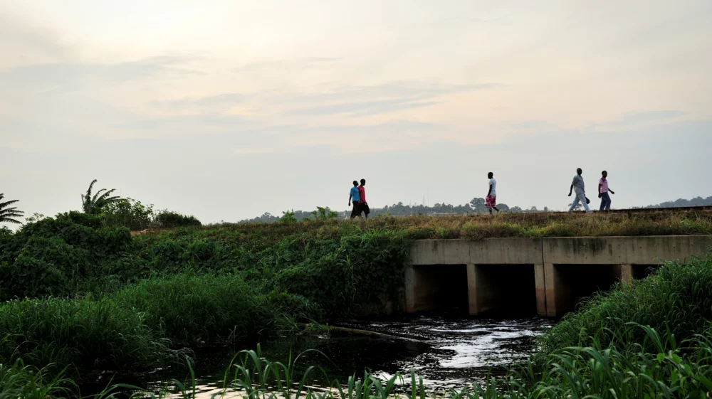 Africans walking on a bridge crossing a wastewater channel in a swamp in Kampala, Uganda