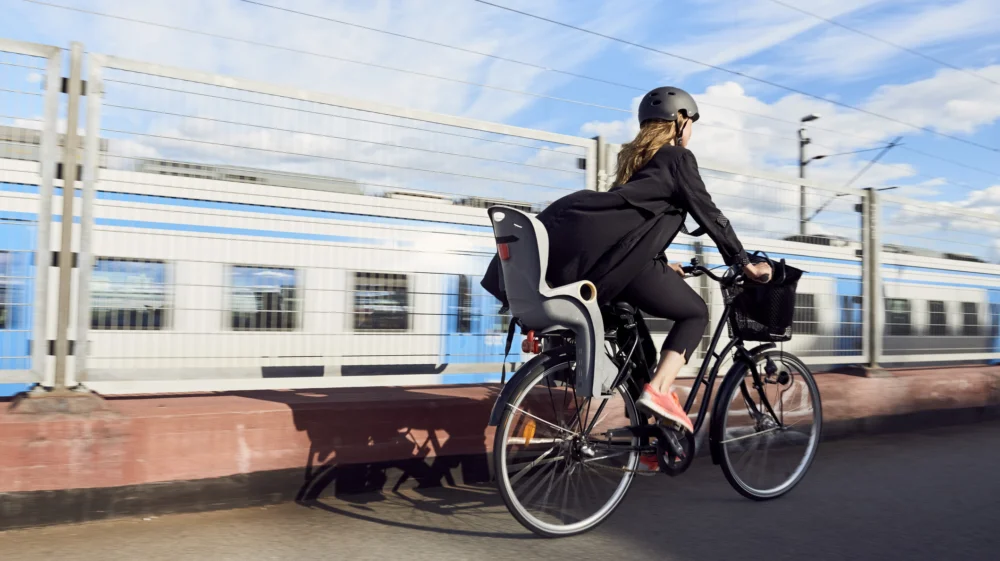 Rear view of mature woman cycling on road by fence against sky