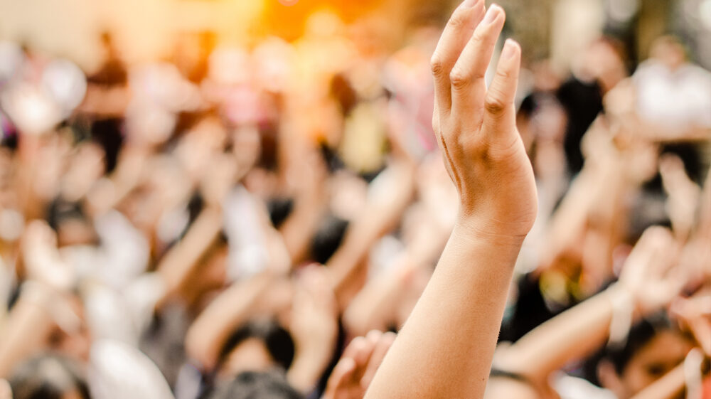 A sea of hands raised, with one hand in focus at the front of the photo