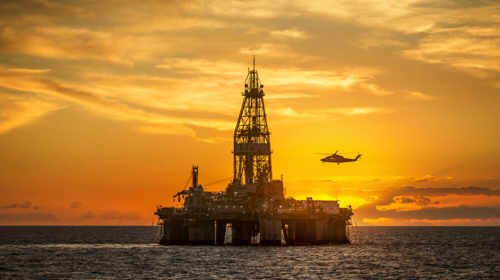 Helicopter flying over Gulf of Mexico oil rig during sunset