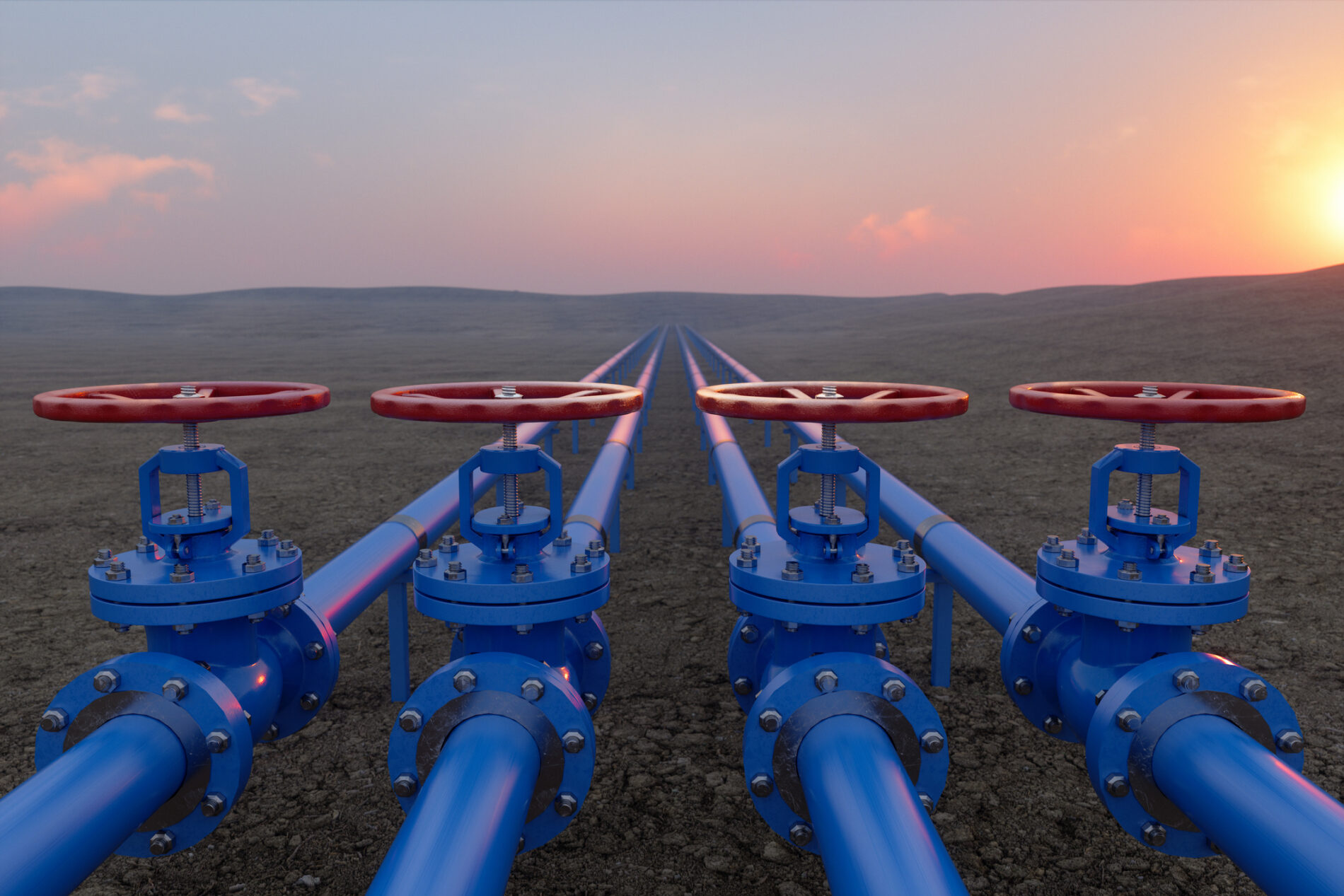 Red and blue gas or oil pipeline valves contrast with an expanse of brown ground against a pink sunset